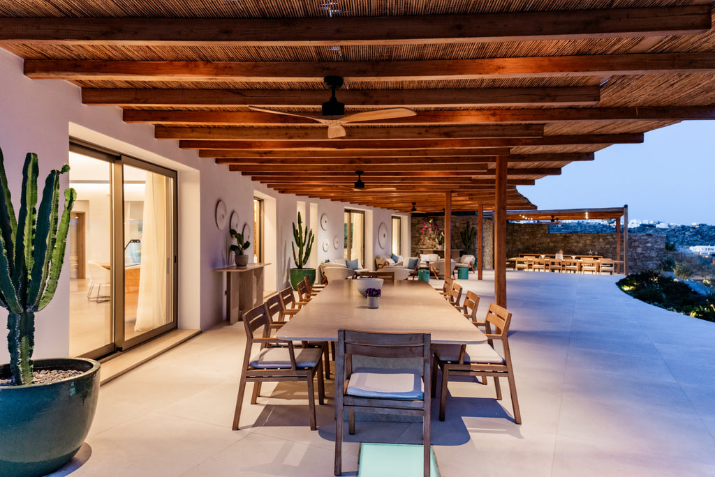 Dining area with wooden table and chairs under a wooden ceiling, overlooking a scenic view.