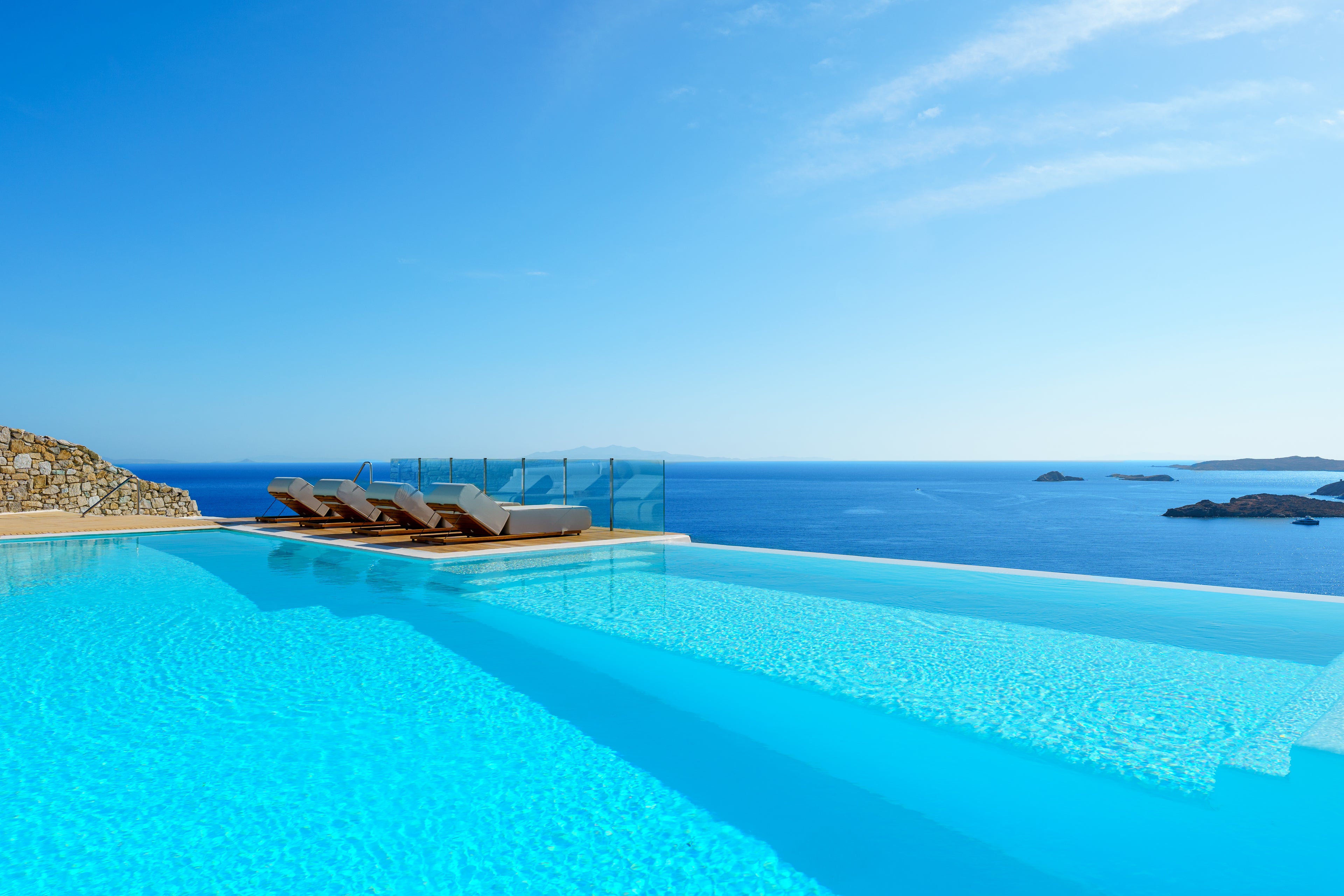 Infinity pool with ocean view and lounge chairs under a clear blue sky.