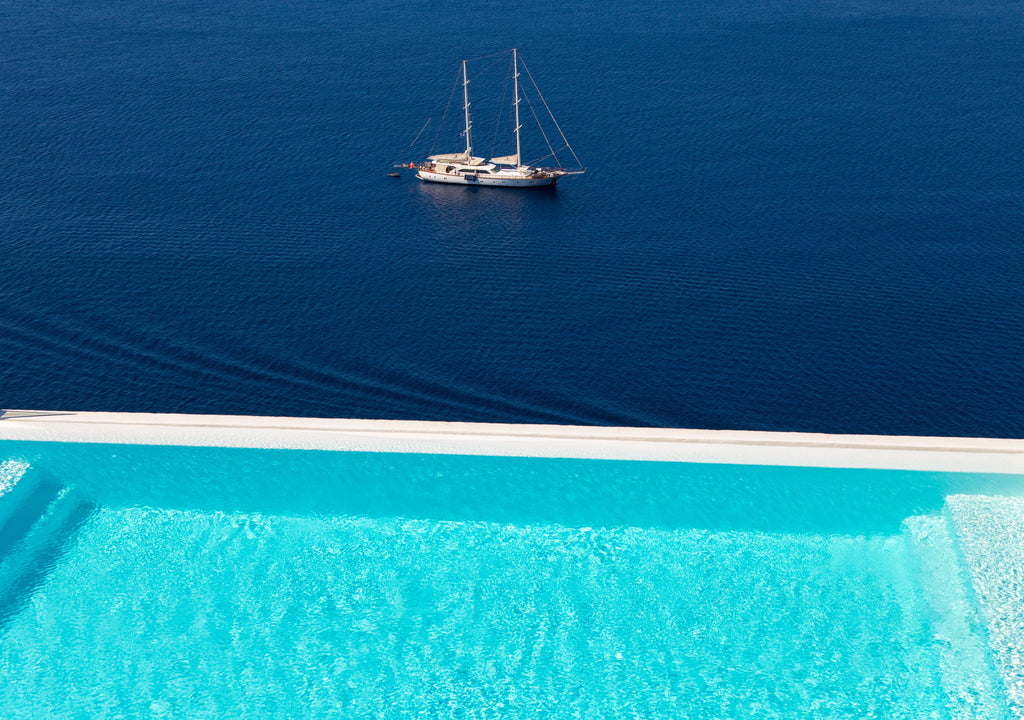 Sailing boat on a vast blue ocean with a pool in the foreground.