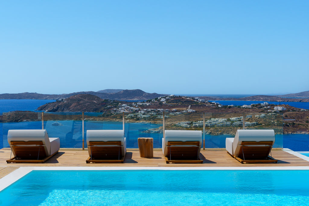 Four lounge chairs by a pool with a scenic view of the sea and islands.