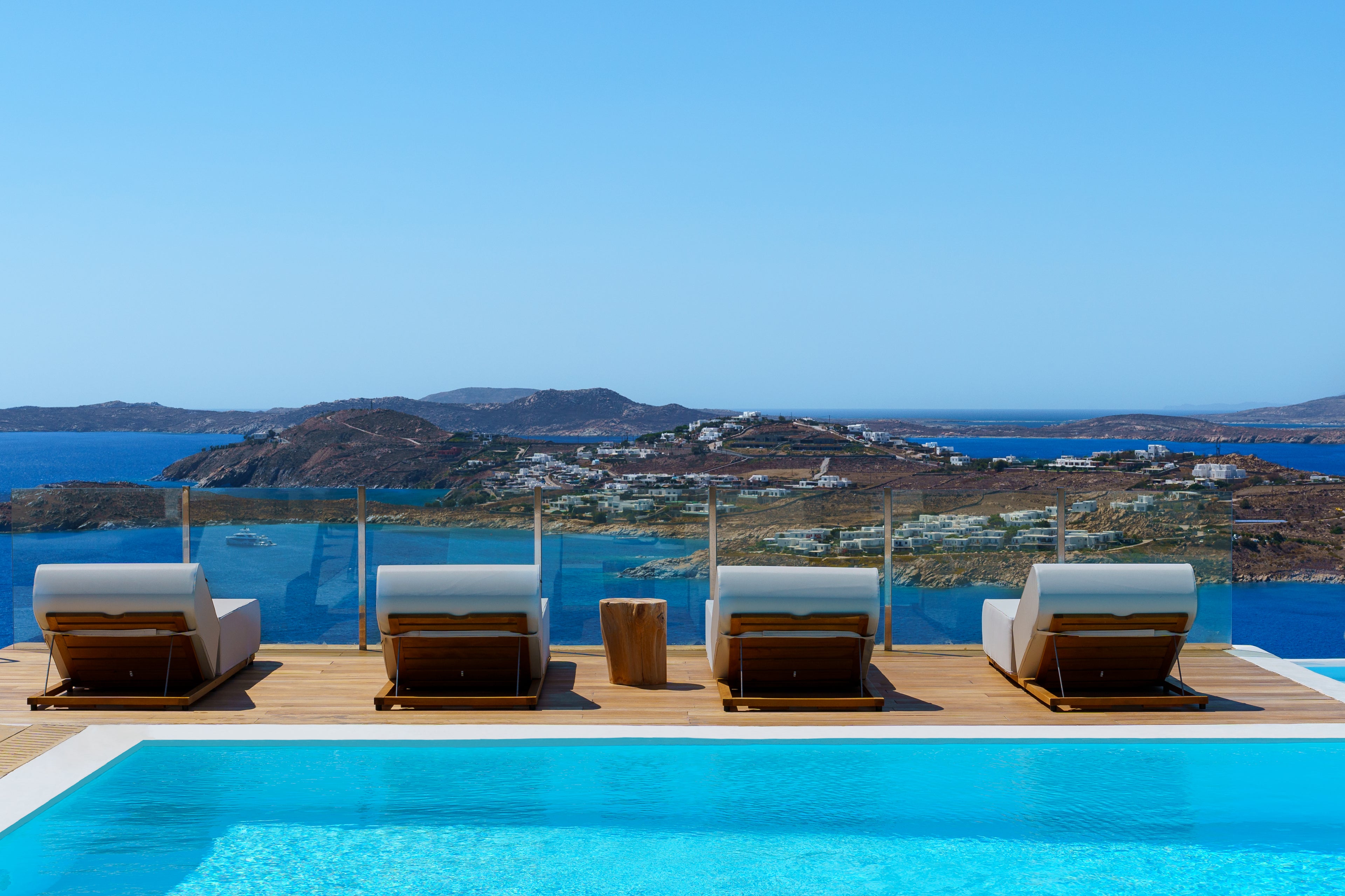Four lounge chairs by a pool with a scenic view of the sea and islands.