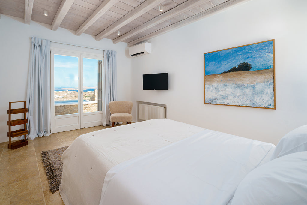 Modern bedroom with a large bed, chair, and wall art overlooking the sea.