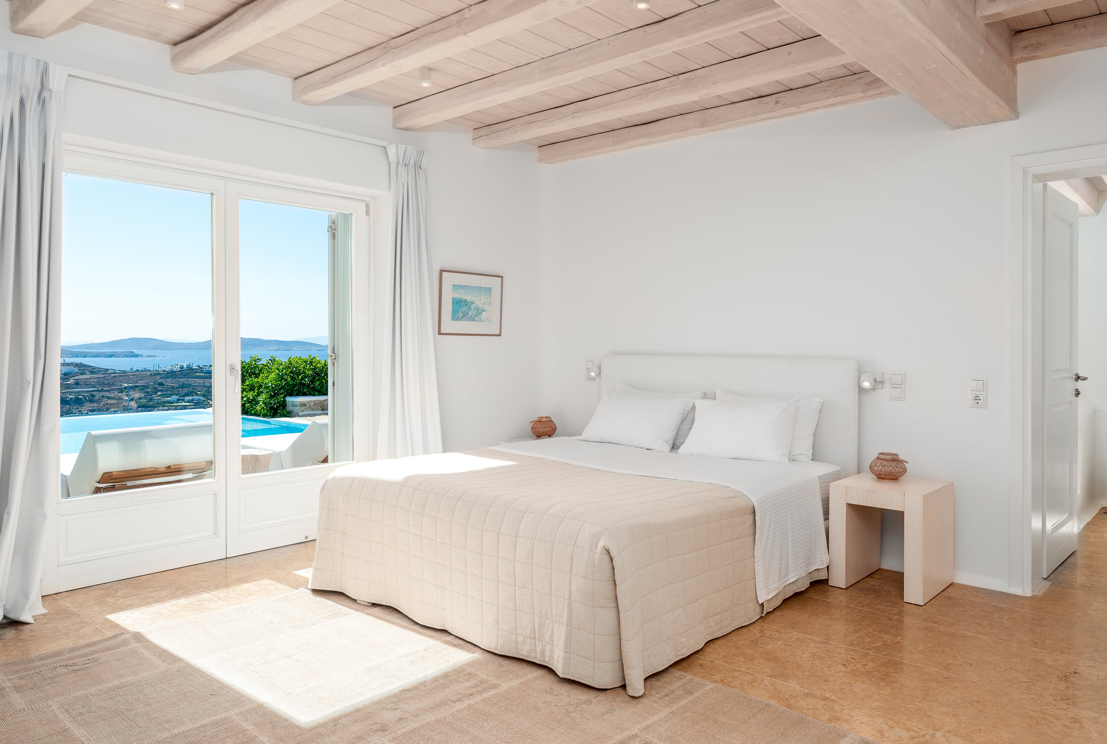 Modern bedroom with a large window, white bed, and wooden beams.
