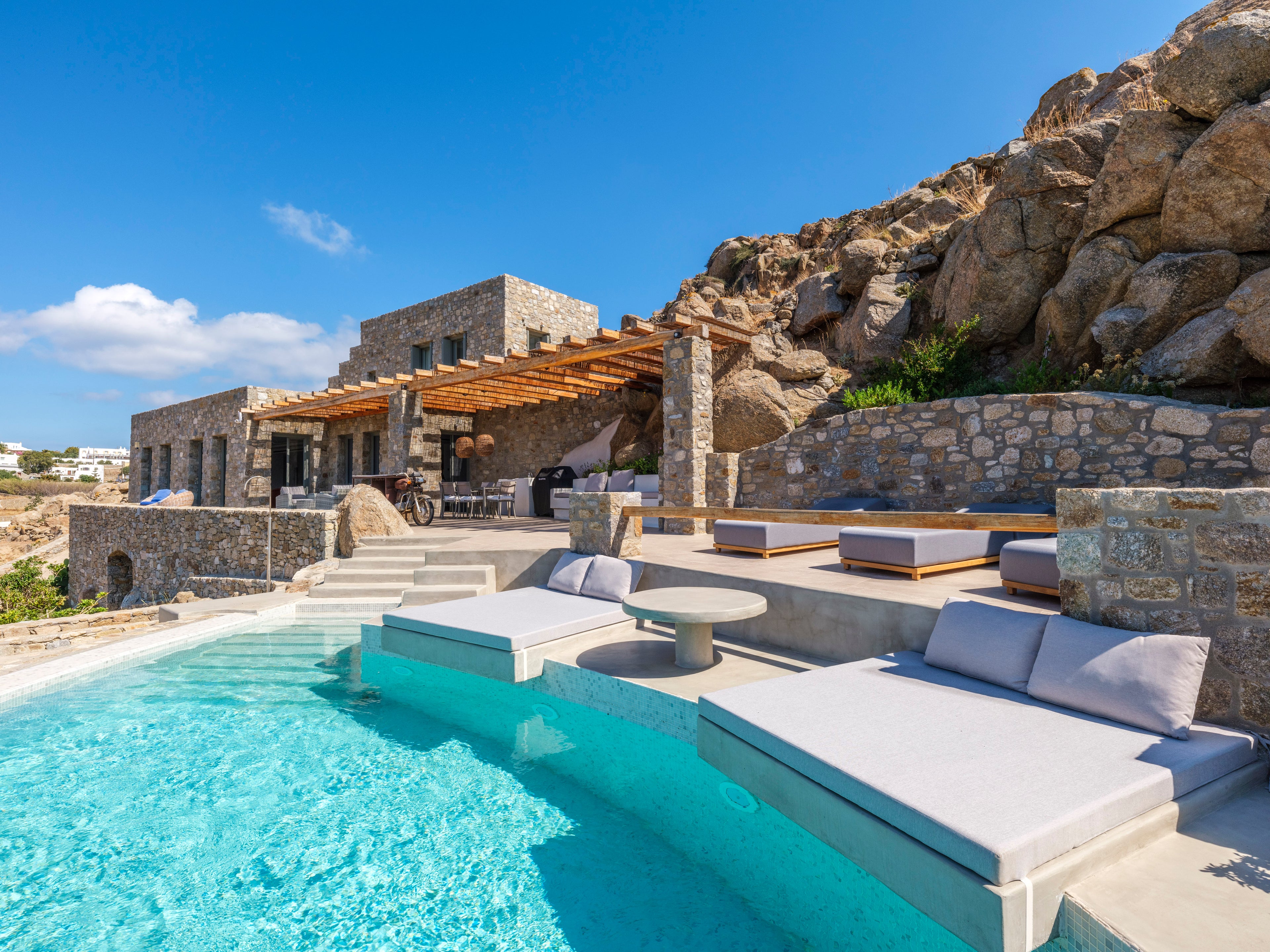 Luxury outdoor pool area with stone walls and modern furniture under a clear blue sky.