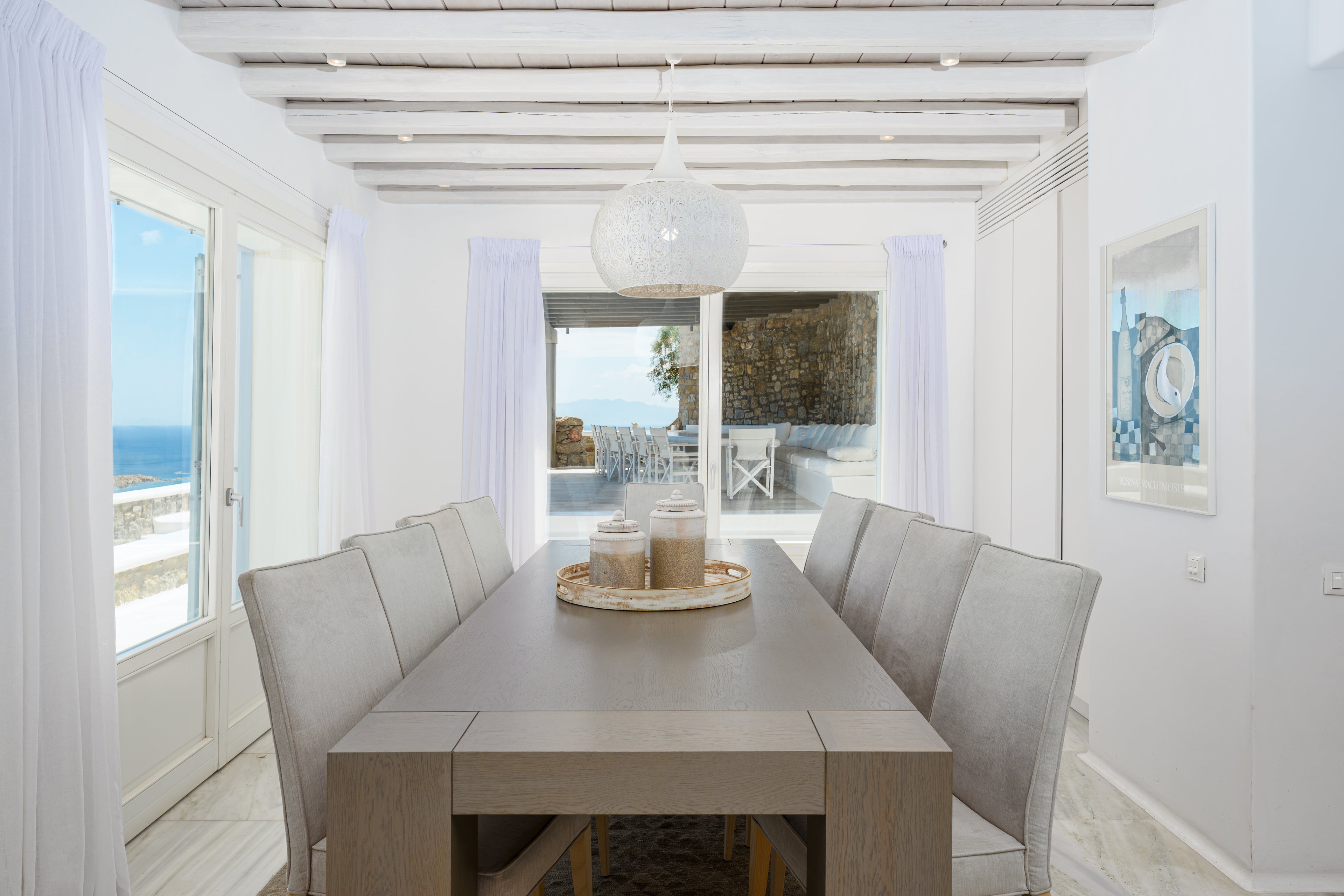 Dining area with a table and chairs in a bright room with large windows overlooking an ocean view.