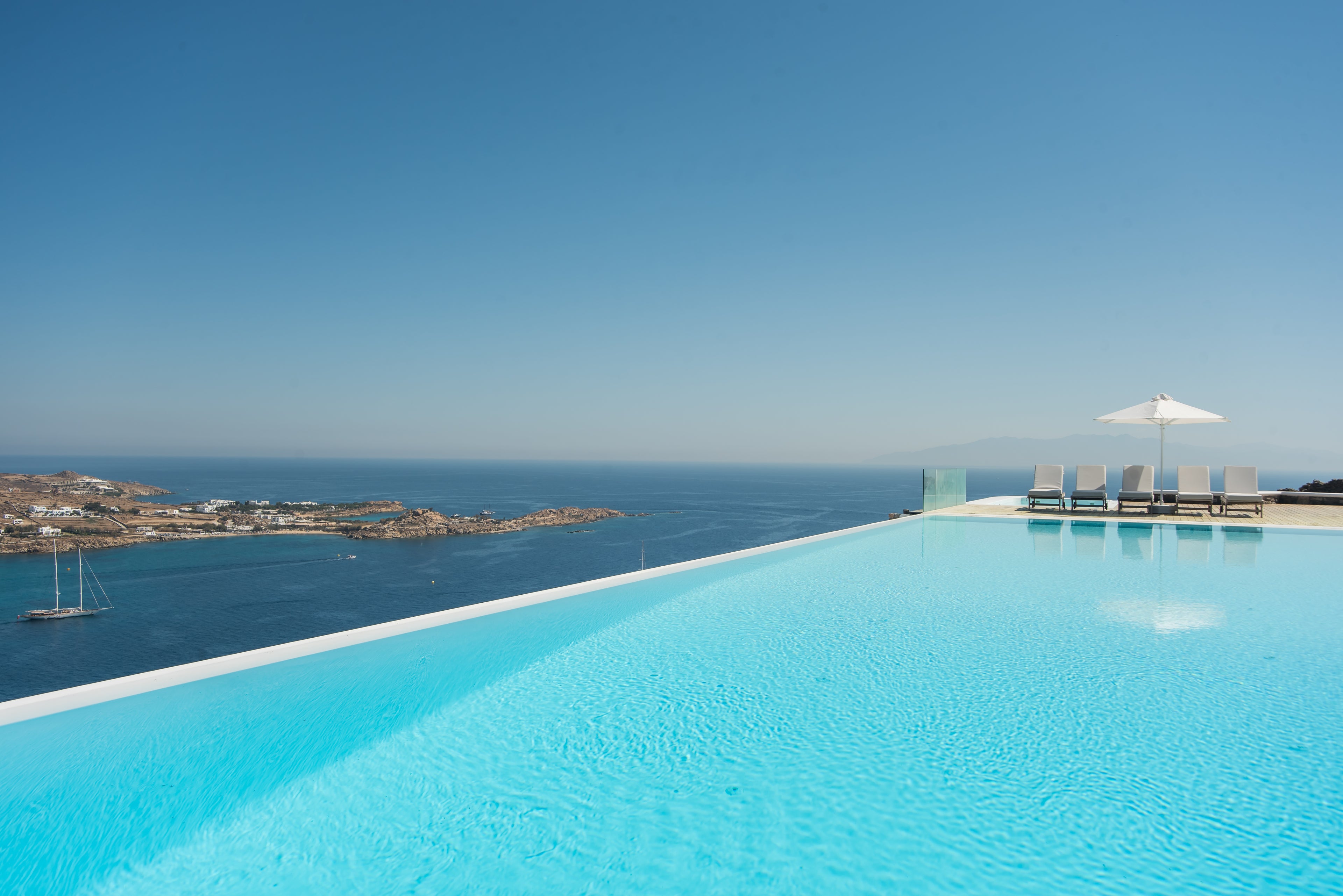 Infinity pool with ocean view and lounge chairs under a clear blue sky