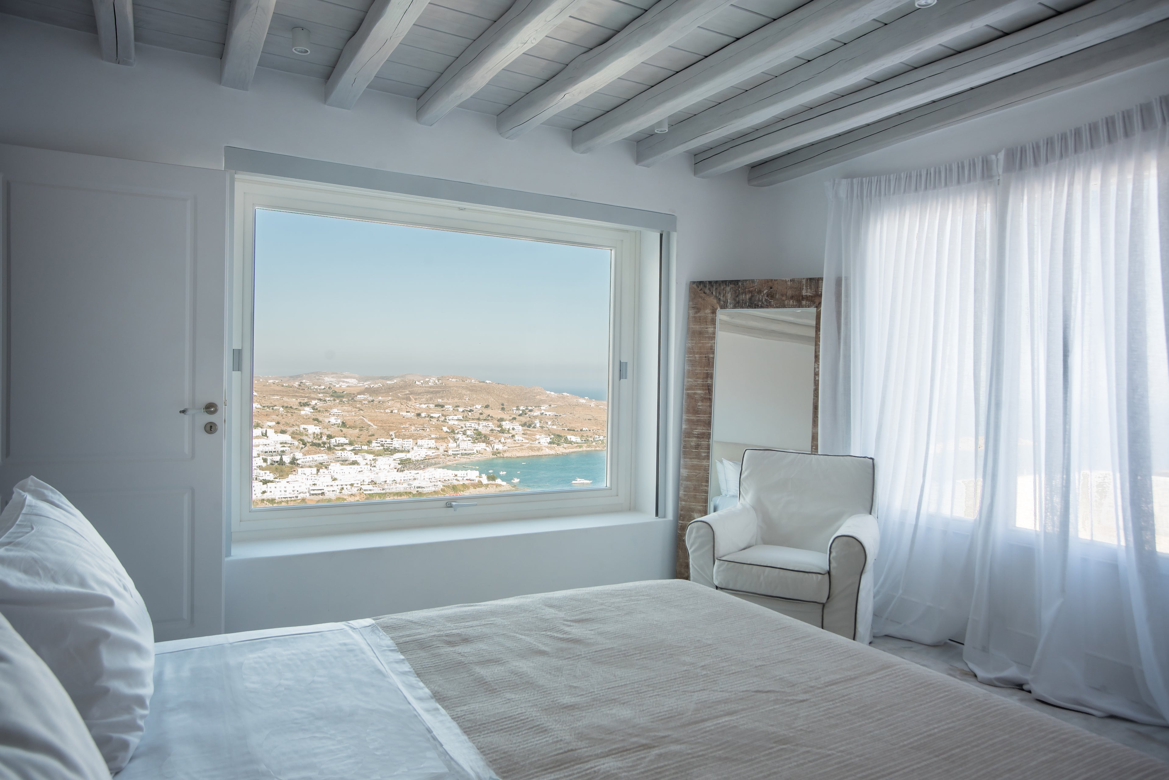 Bedroom with large window offering a view of a coastal town.