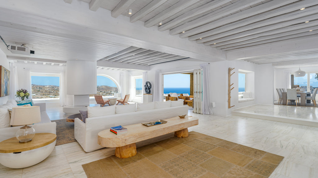 Modern living room with white walls, wooden coffee table, and large windows overlooking the ocean.