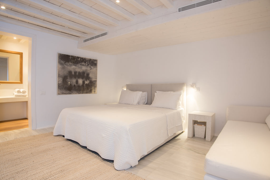 Modern bedroom with white bed, nightstands, and artwork on a white wall.