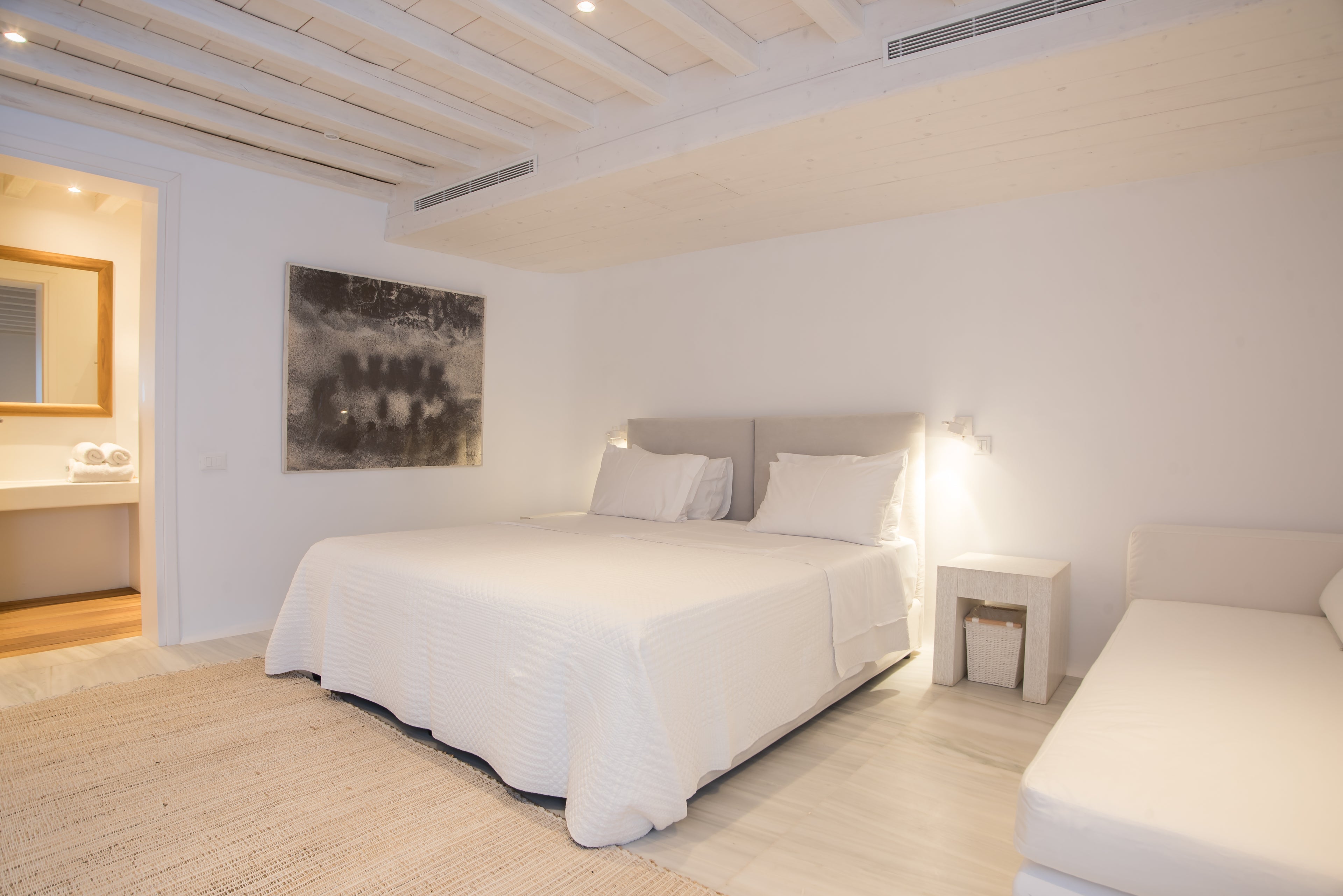Modern bedroom with white bed, nightstands, and artwork on a white wall.