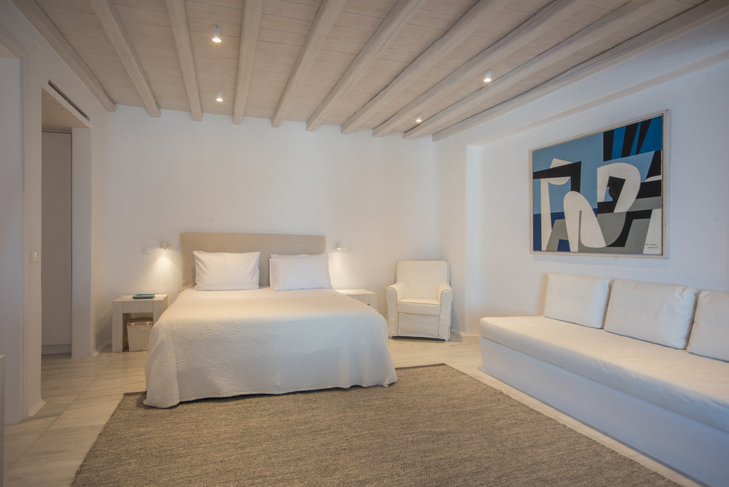 Modern bedroom with white bed, sofa, and abstract art on wall.