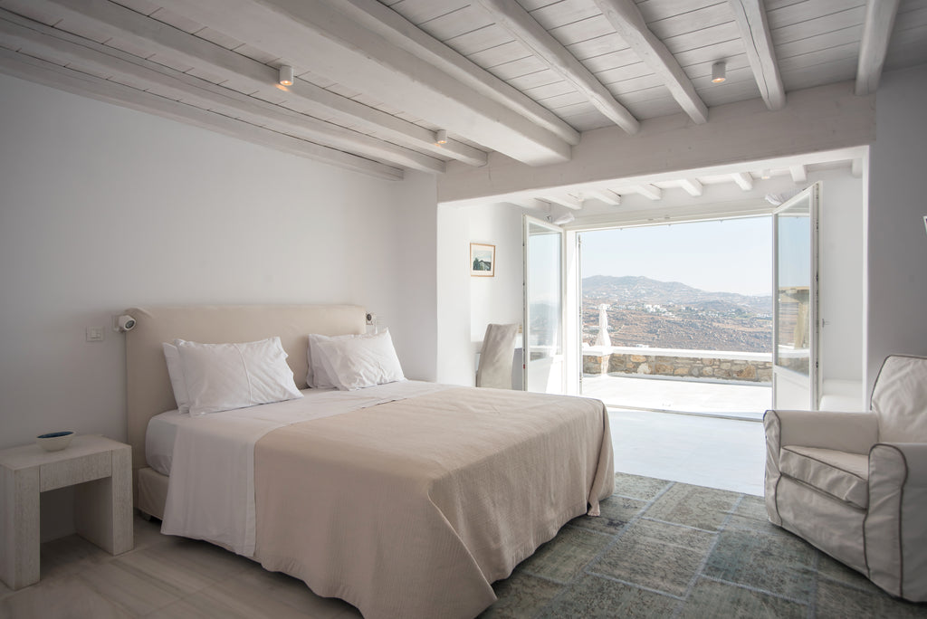 Neatly made bed in a bedroom with a view of mountains through large windows.