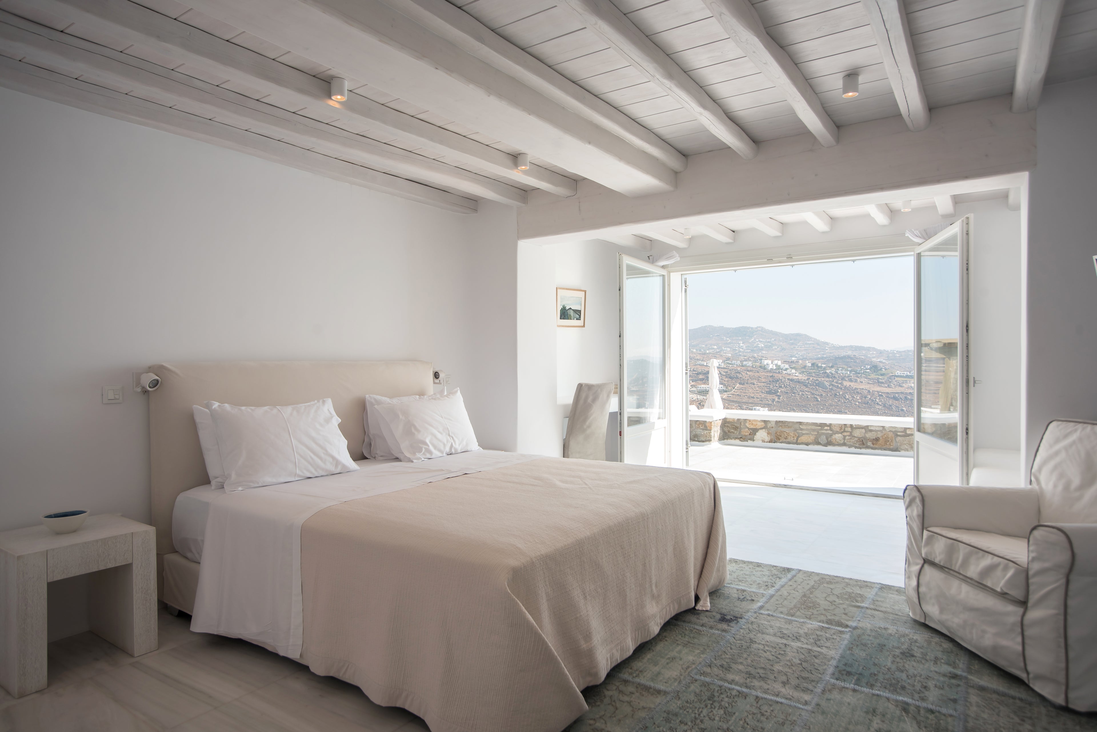 Neatly made bed in a bedroom with a view of mountains through large windows.