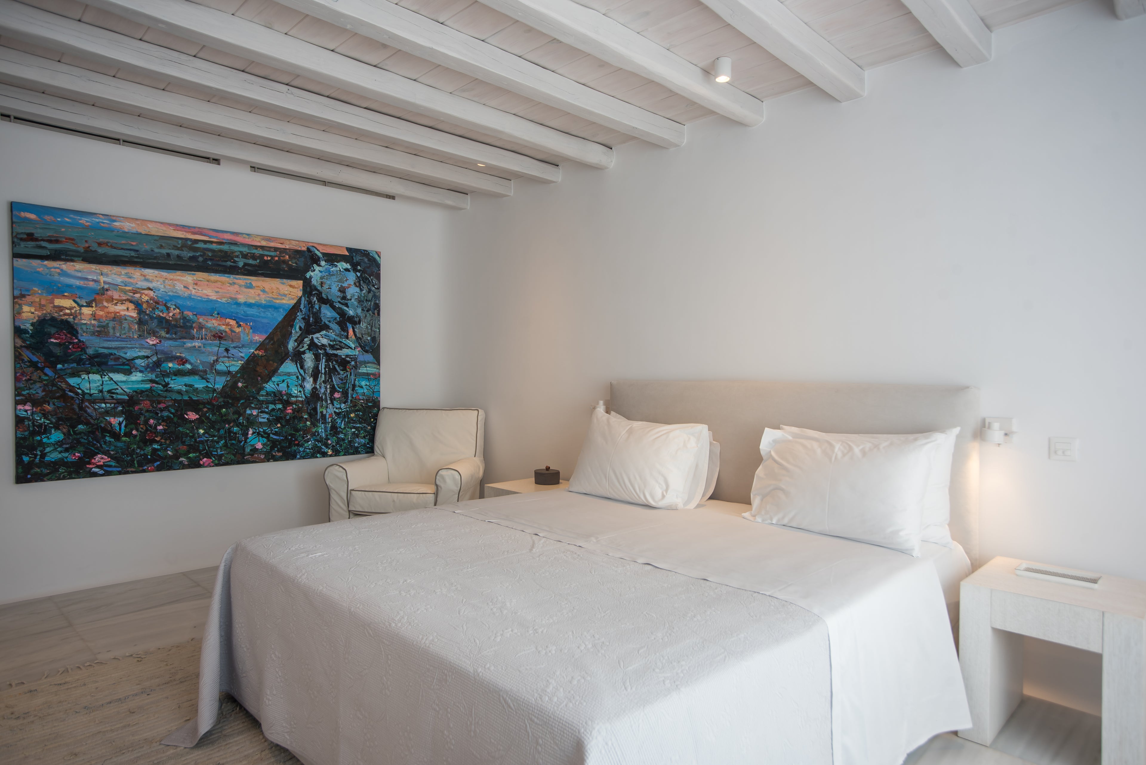 Neatly made bed in a room with a large painting on the wall.