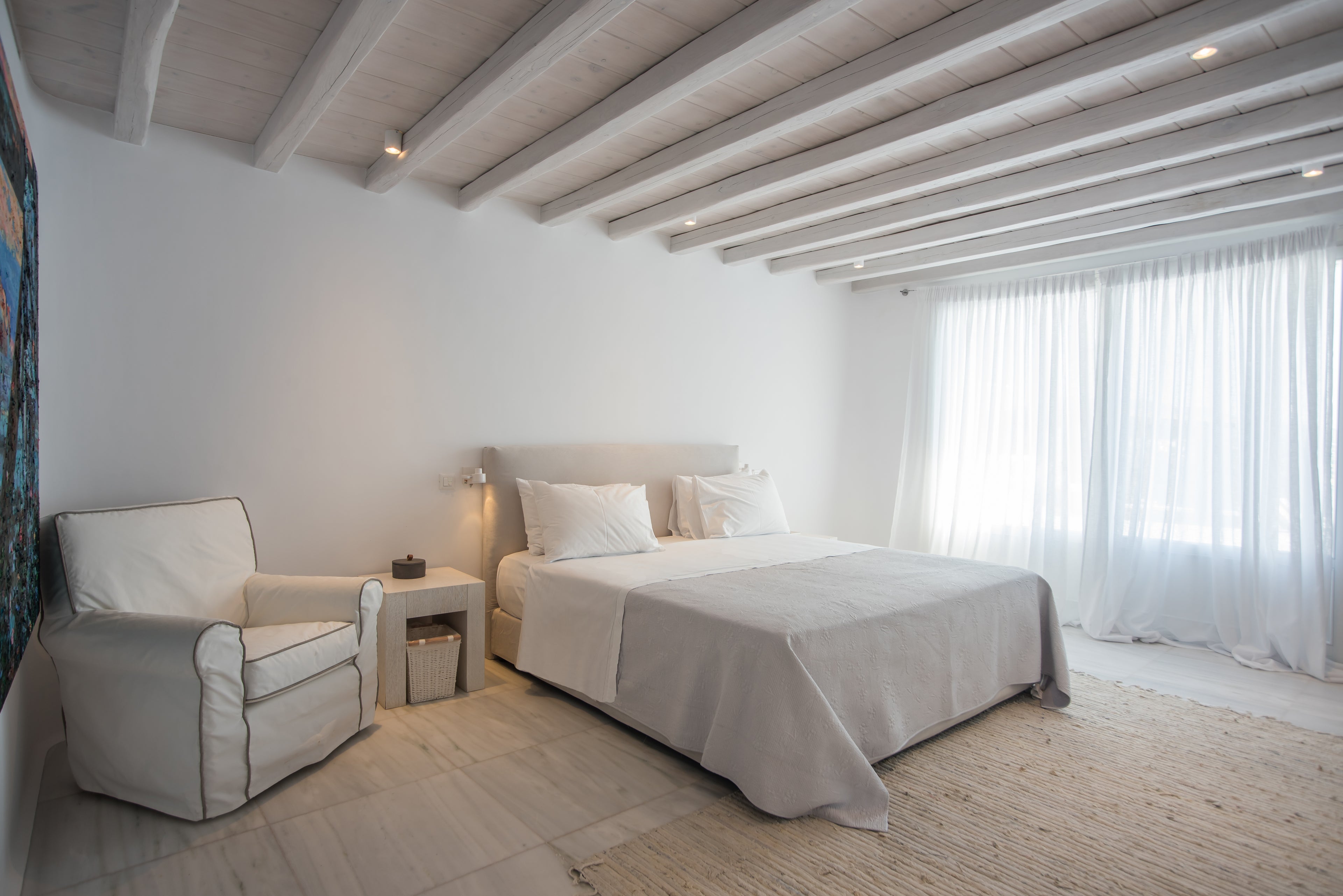 Modern bedroom with white bed, chair, and ceiling beams