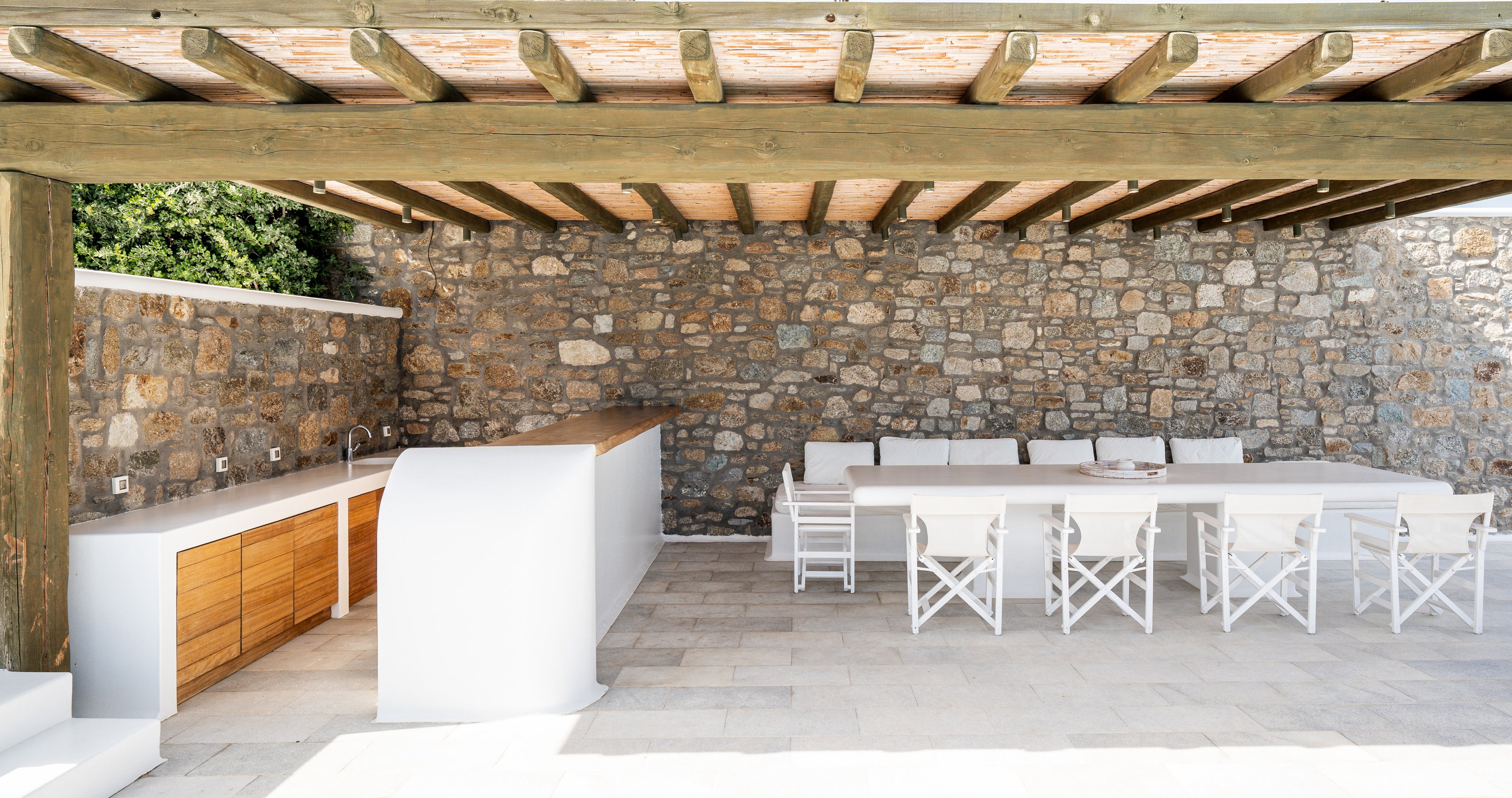 Outdoor kitchen and dining area with stone wall and wooden pergola