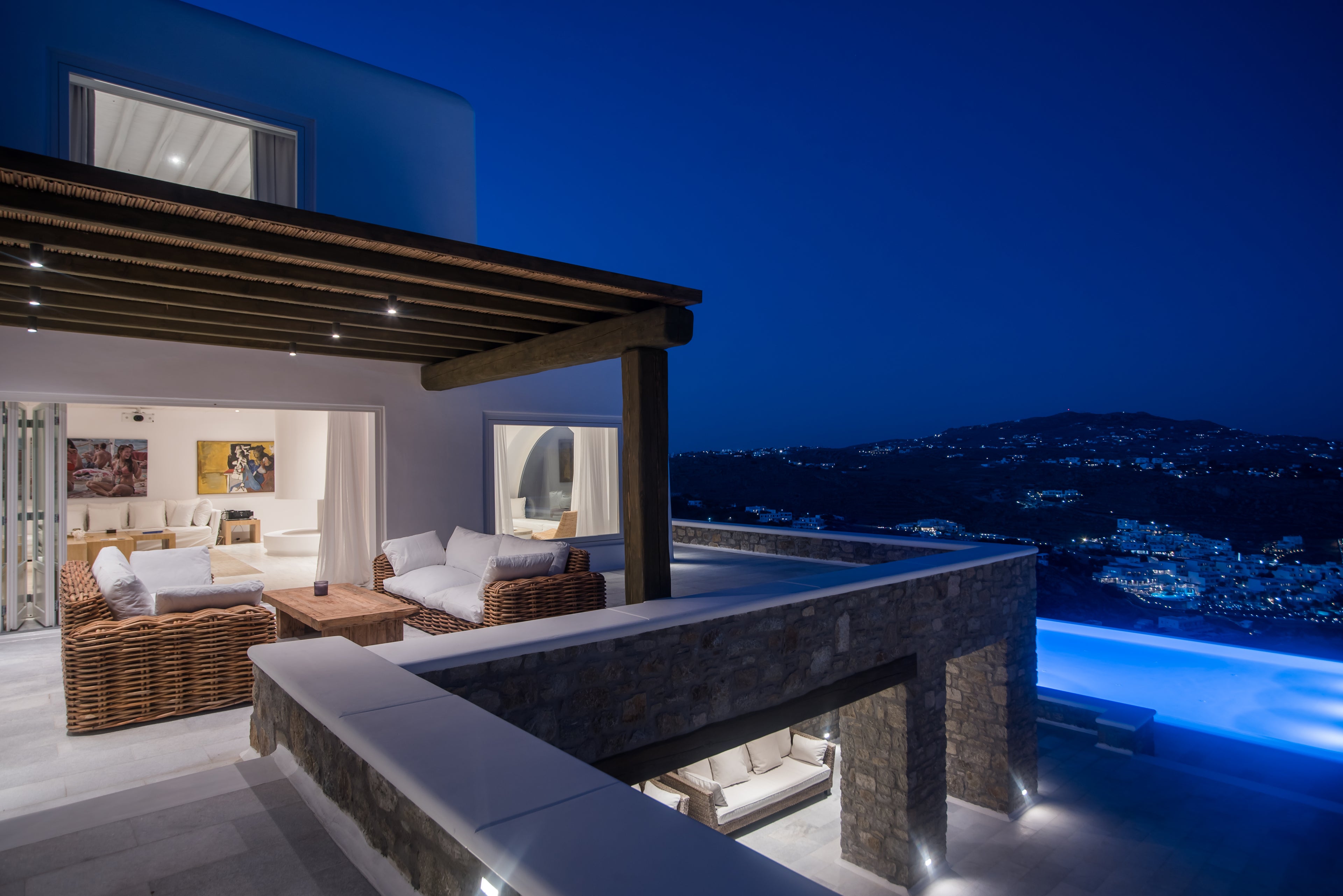 Luxury outdoor living area with pool at night, overlooking a scenic landscape.