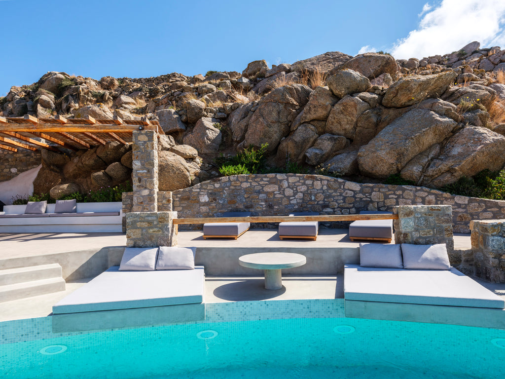 Outdoor seating area with a pool, stone walls, and large rocks in the background.
