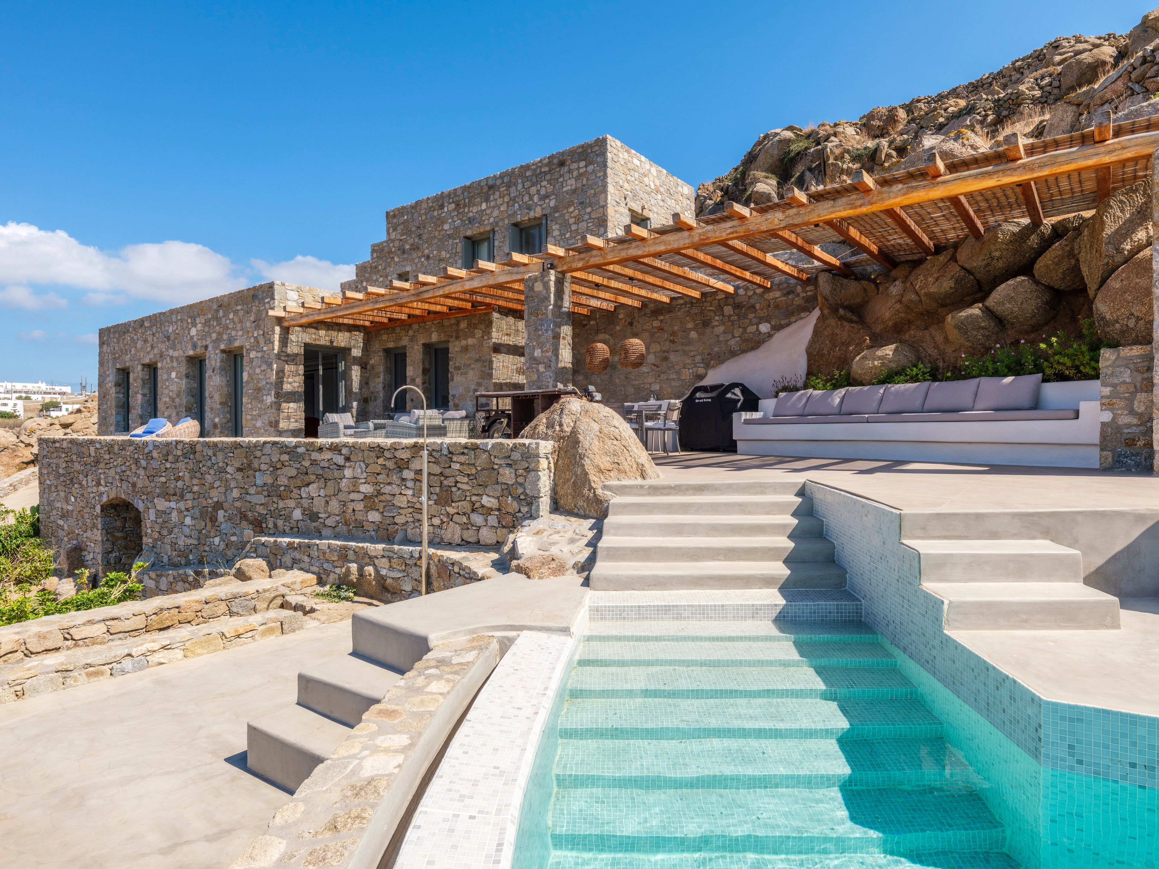 Luxury villa with stone exterior, wooden pergola, and pool area.