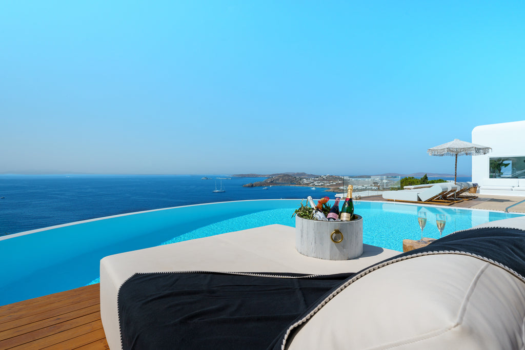 Infinity pool with ocean view, lounge chairs, and a table with drinks.