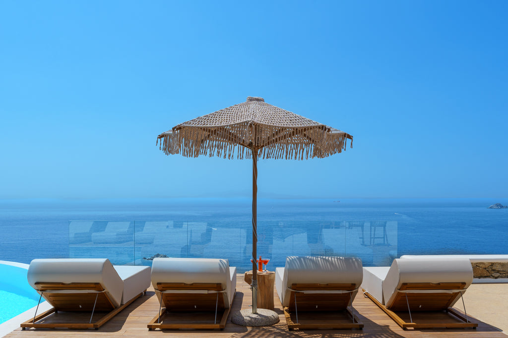 Beach chairs with a woven umbrella by a pool with ocean view