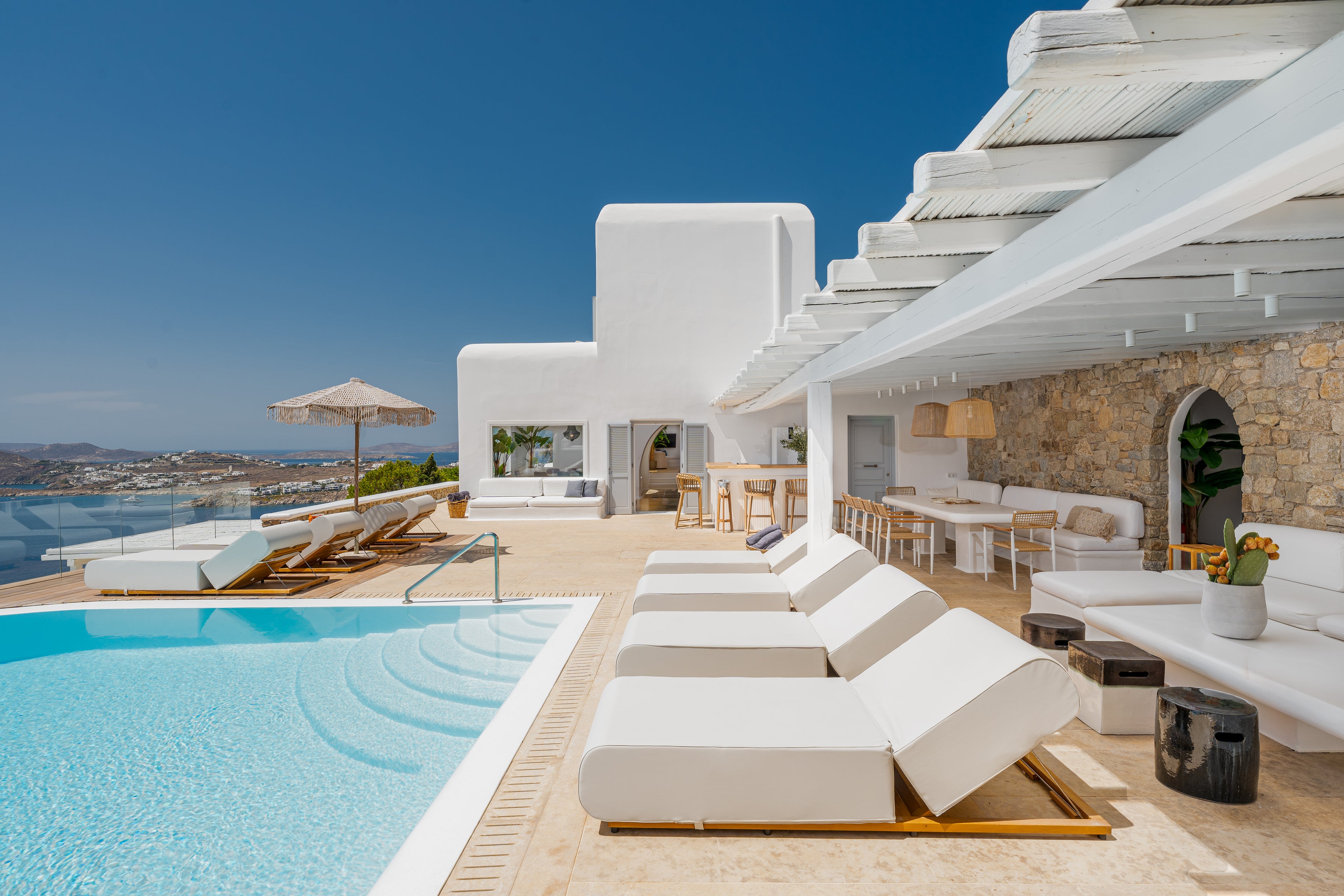 Luxury outdoor pool area with white lounge chairs and a clear blue sky.