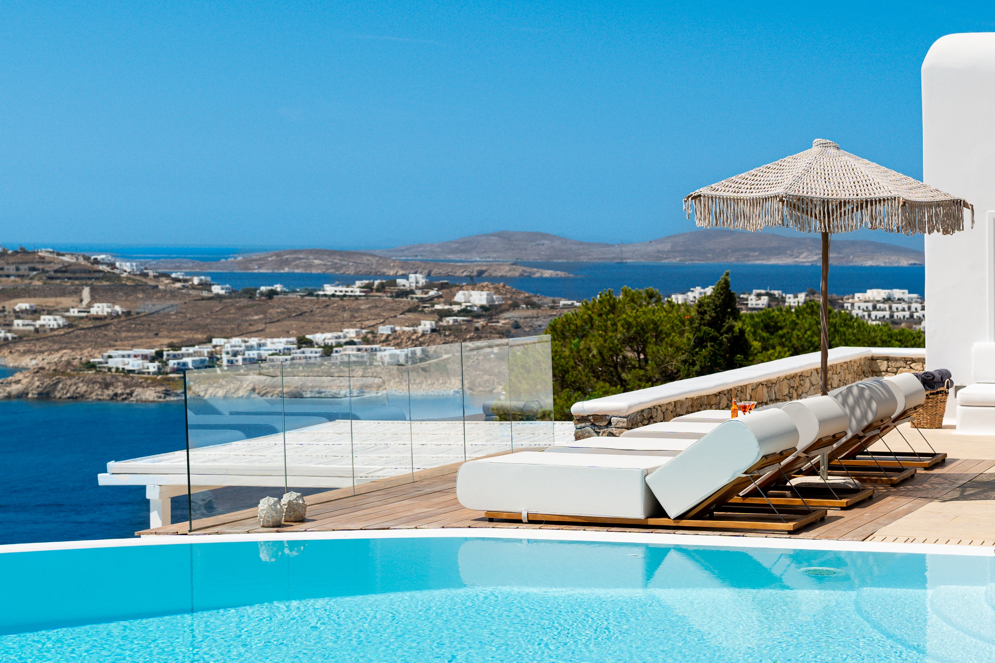 Pool area with lounge chairs and an umbrella overlooking a scenic view of the sea and coastline.