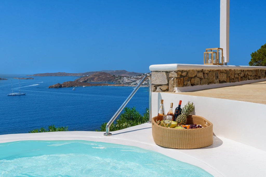 Outdoor setting with a pool, basket of fruit and bottles, and ocean view.