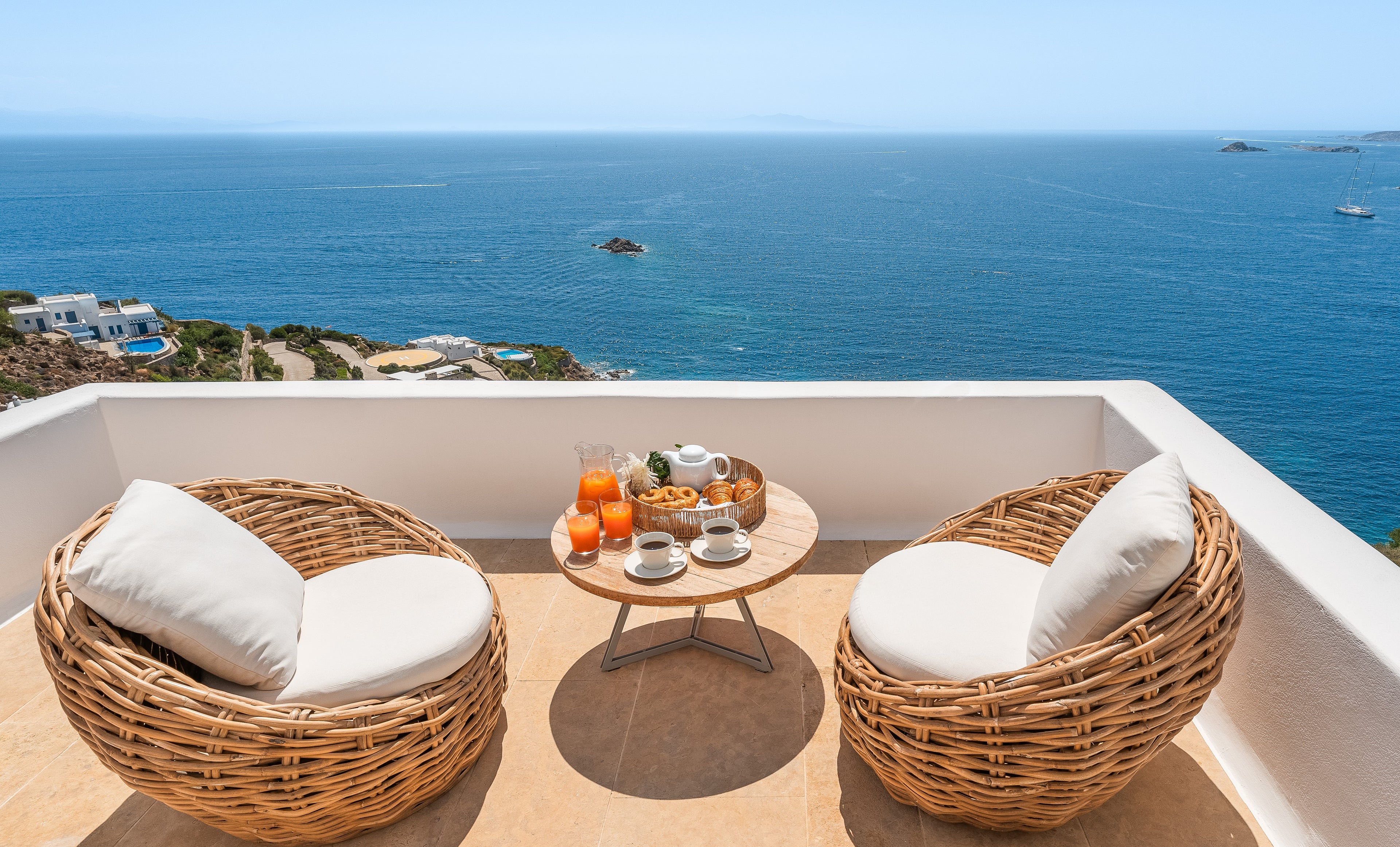 Two wicker chairs with white cushions on a balcony overlooking the ocean.