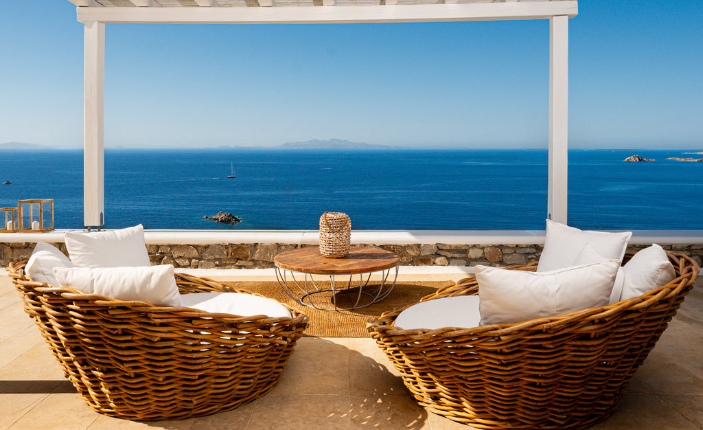 Wicker furniture with white cushions on a patio overlooking the ocean.