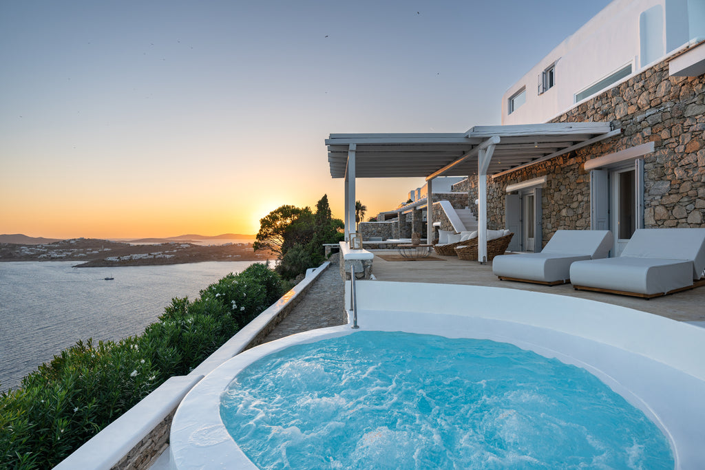 Outdoor hot tub with a scenic view of a house and water at sunset.