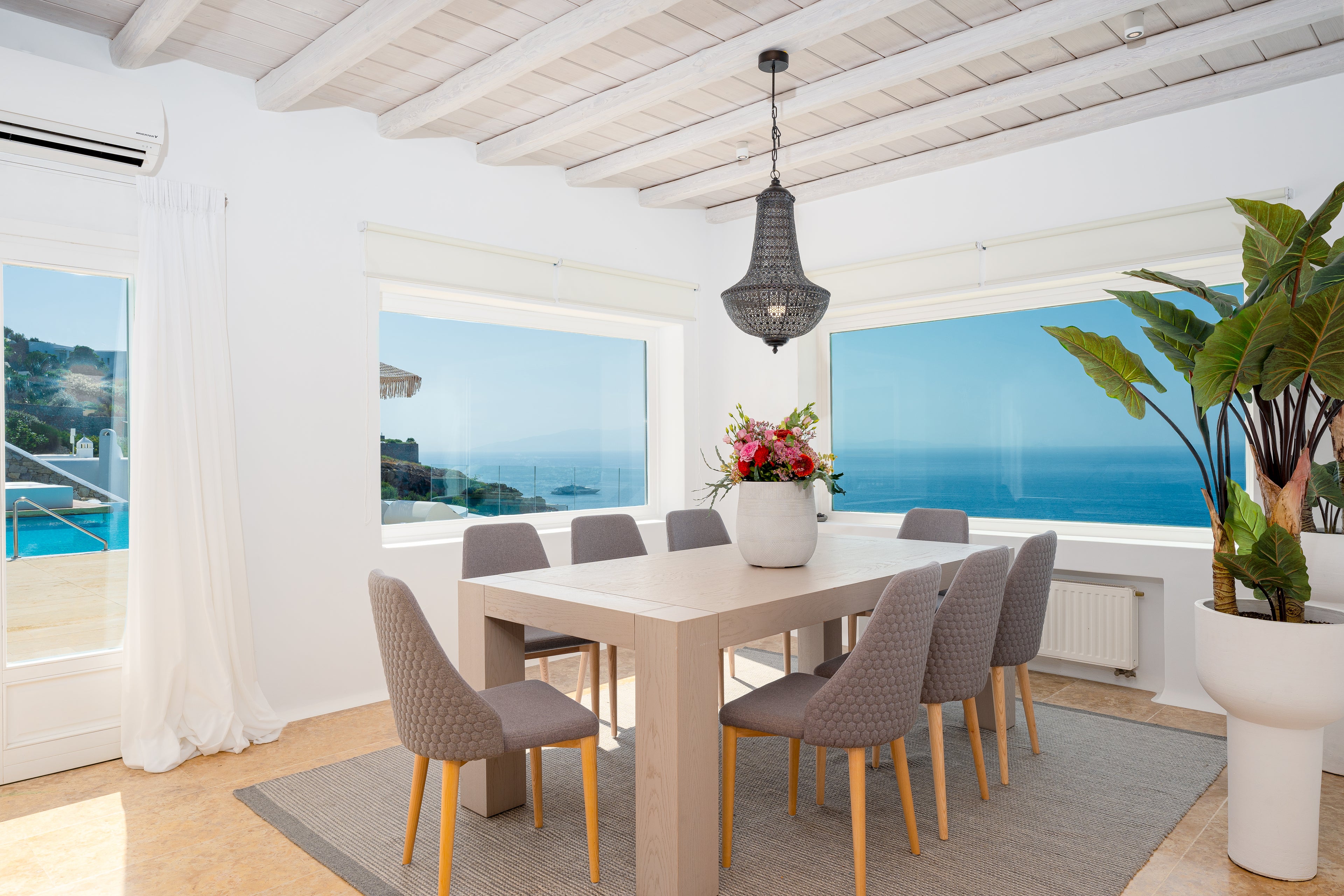 Dining area with a table and chairs in a room with large windows overlooking the ocean.