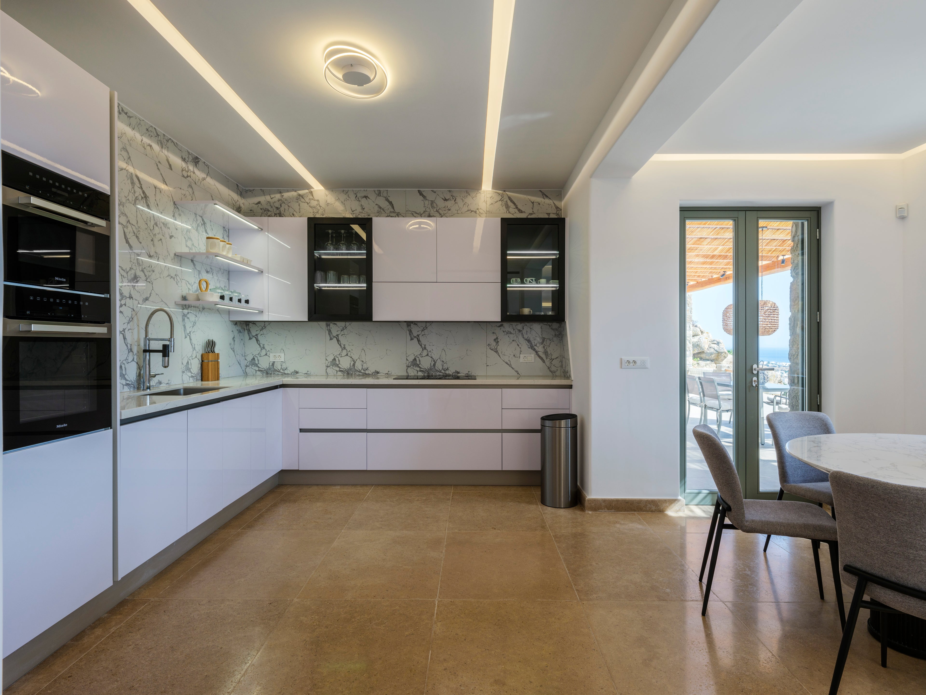 Modern kitchen with white cabinets, marble countertops, and a dining area.