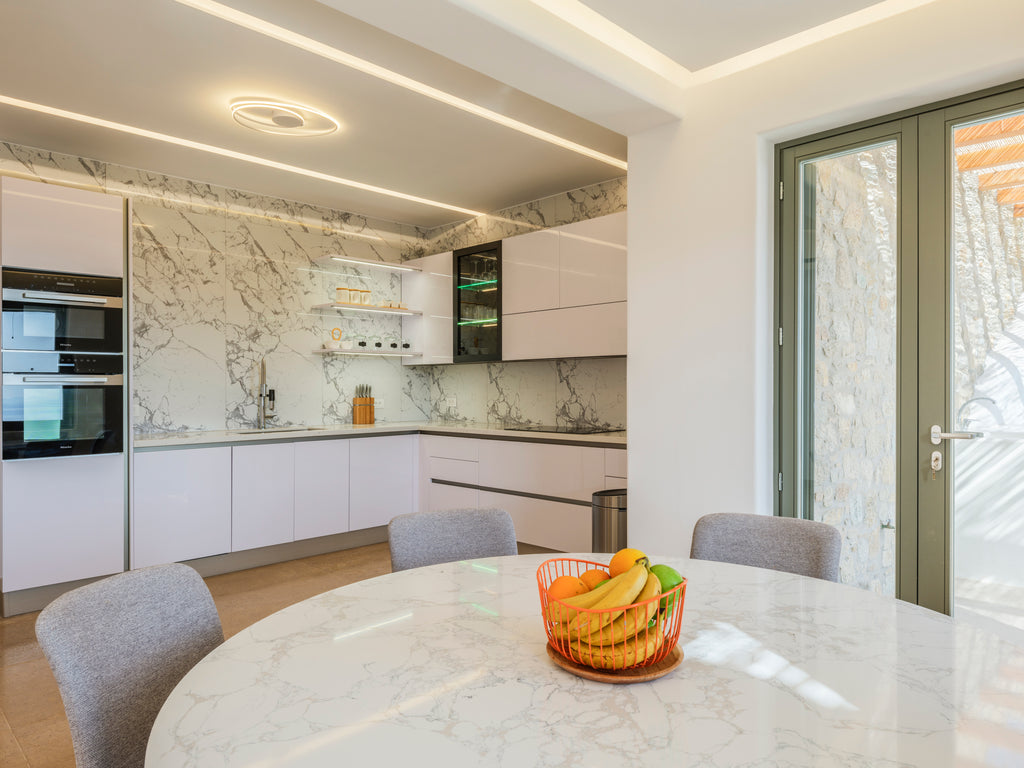Modern kitchen with marble countertops and a dining area with fruit bowl.