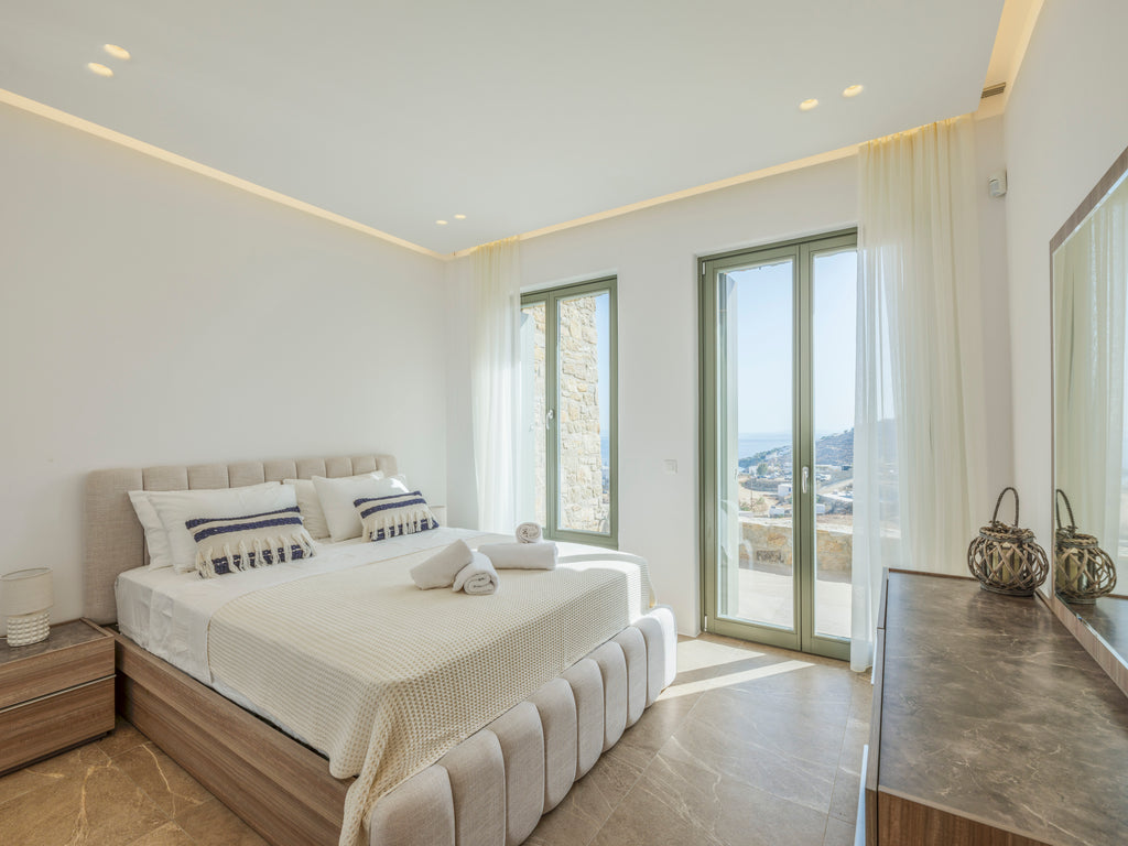 Modern bedroom with a large bed, nightstands, and a view of the sea through a window.