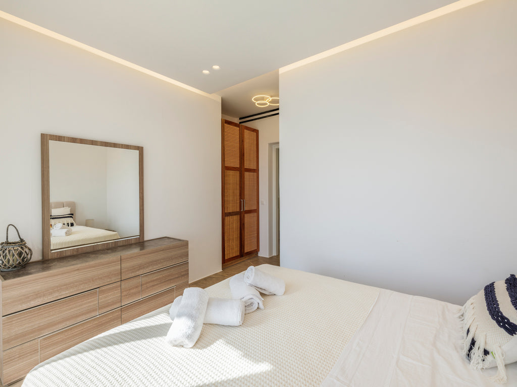 Modern bedroom with wooden dresser, mirror, and bed with white bedding.
