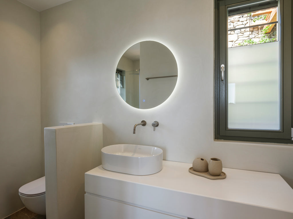Modern bathroom with round illuminated mirror and white sink.