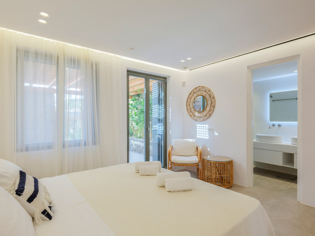 Modern bedroom with a bed, chair, and bathroom in the background.