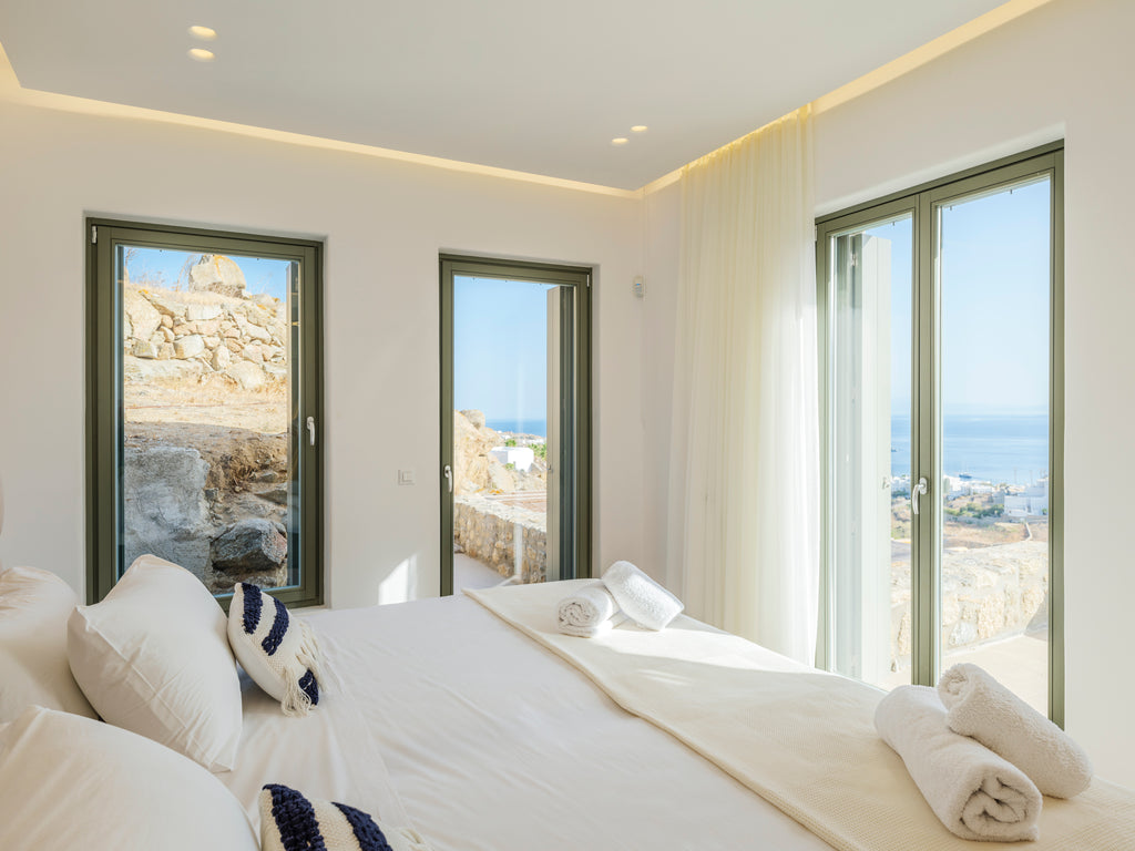 Modern bedroom with white bedding and large windows overlooking a scenic view.