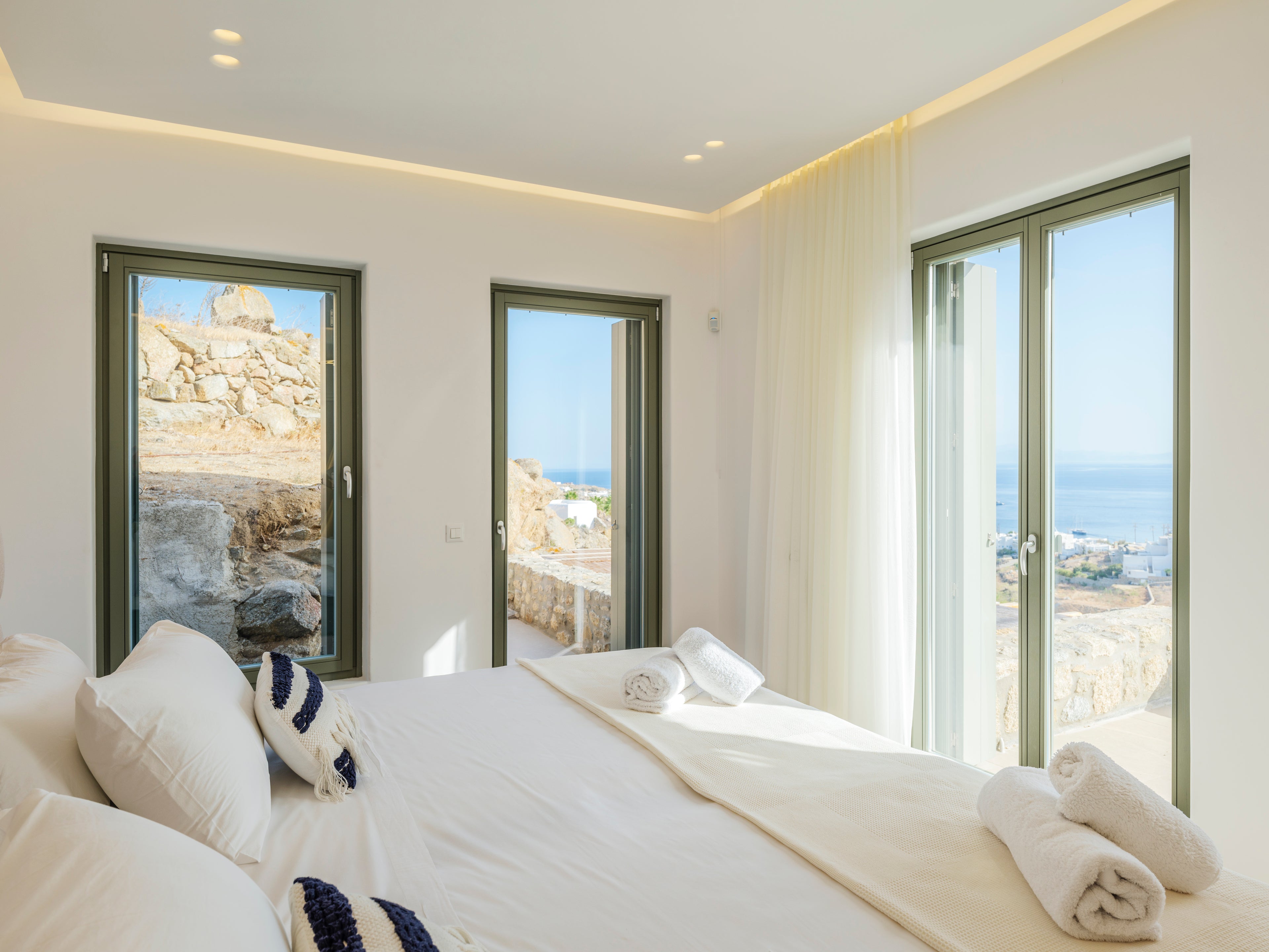 Modern bedroom with white bedding and large windows overlooking a scenic view.