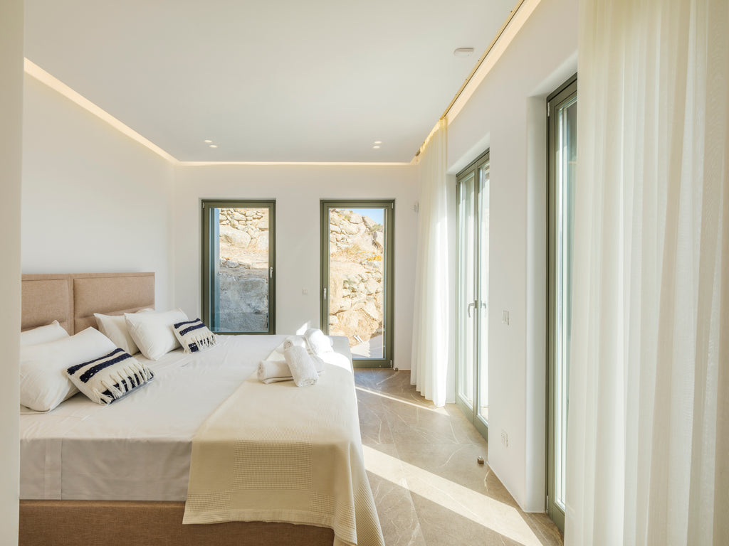 Modern bedroom with a bed, pillows, and large windows.