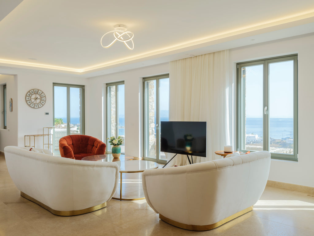 Modern living room with white furniture, large windows, and a view of the sea.