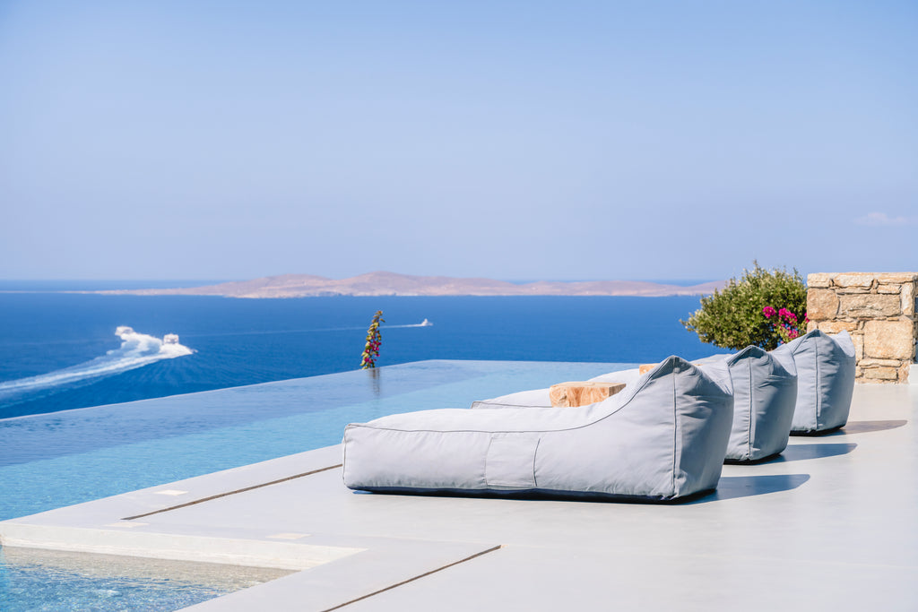 Outdoor lounge area with gray cushions by a pool overlooking the ocean.