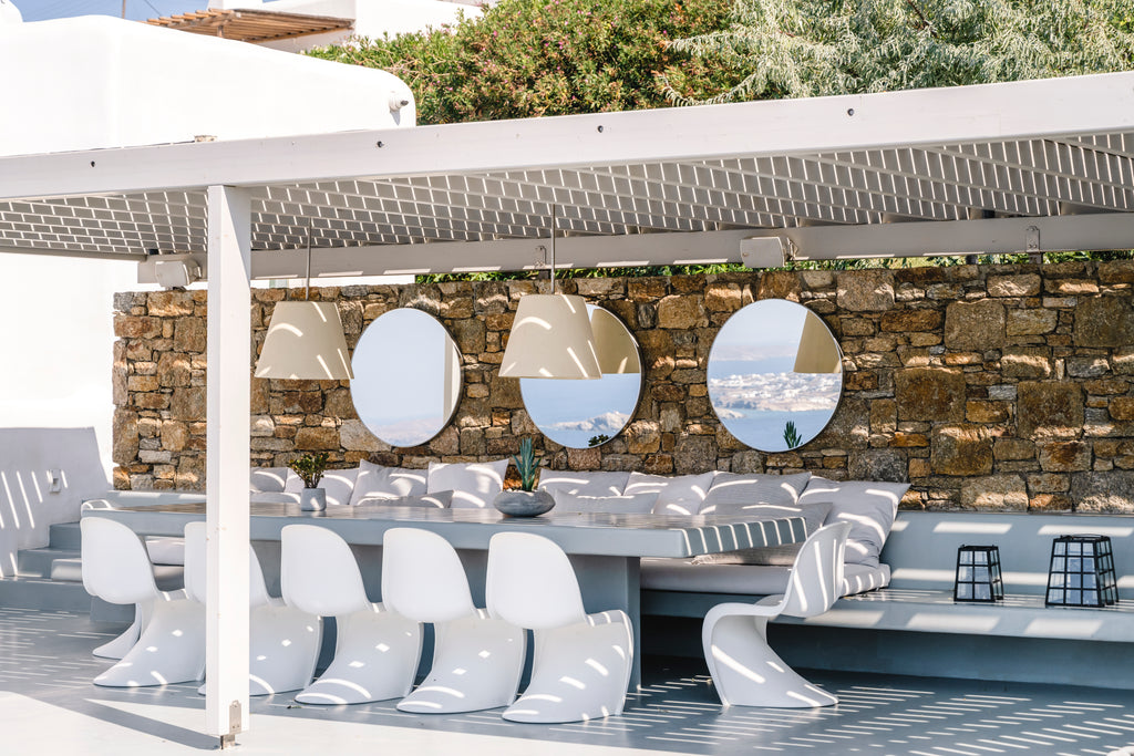 Outdoor seating area with modern white chairs and tables against a stone wall.