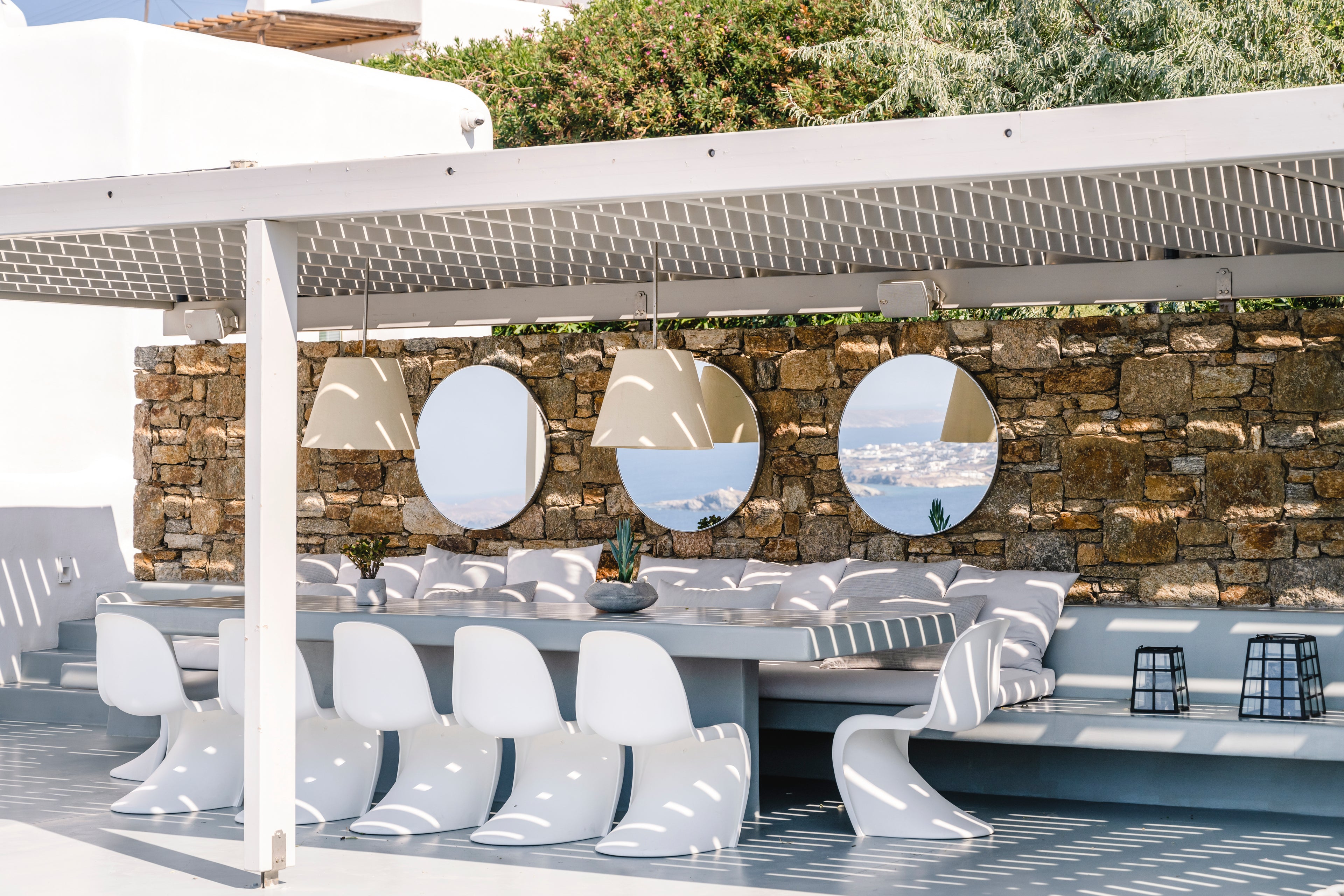 Outdoor seating area with modern white chairs and tables against a stone wall.