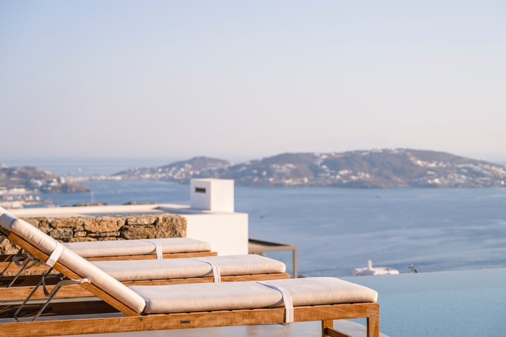 Two lounge chairs with cushions on a balcony overlooking a scenic ocean view with mountains in the background.