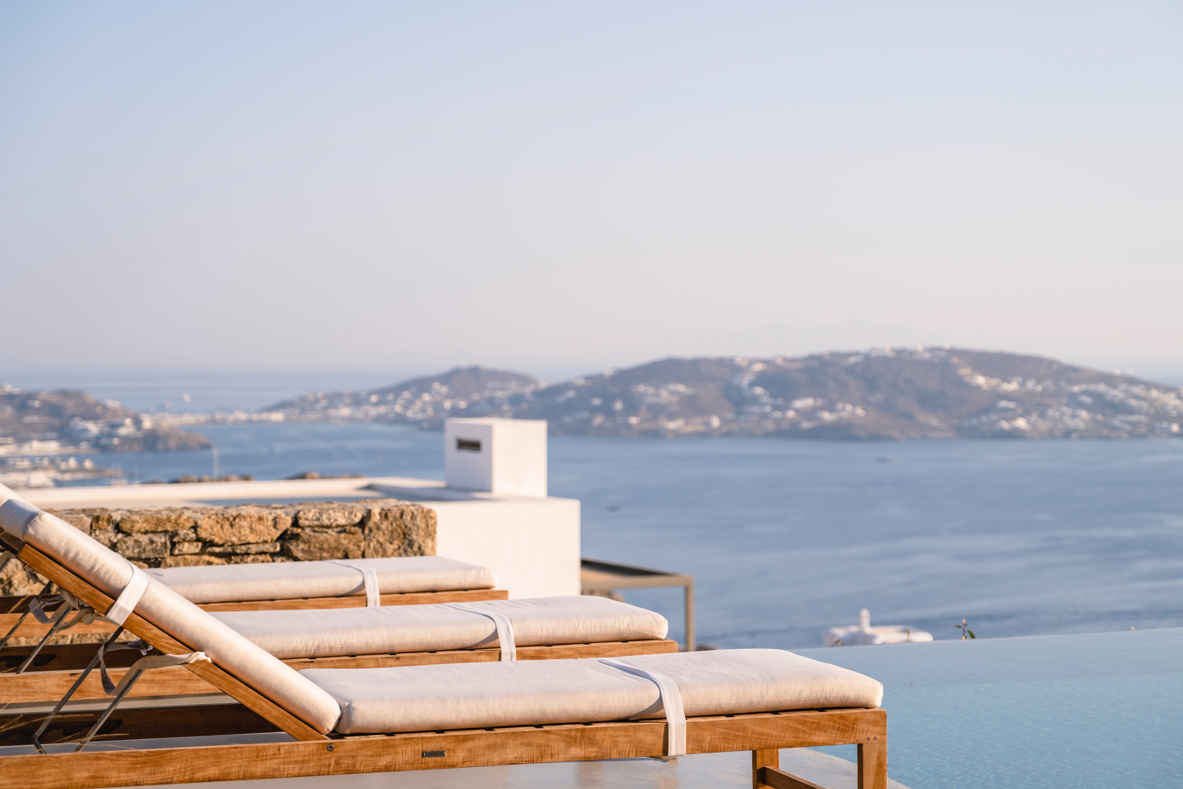 Two lounge chairs with cushions on a balcony overlooking a scenic ocean view with mountains in the background.