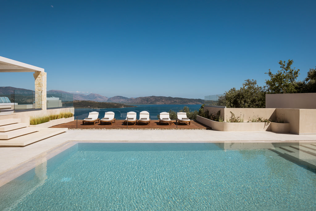 Pool area with lounge chairs and a scenic view of mountains and water.