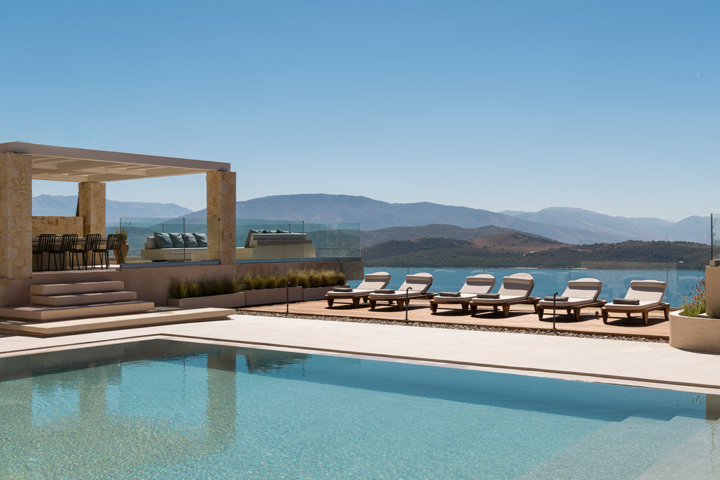 Pool area with lounge chairs and a scenic view of mountains and water.