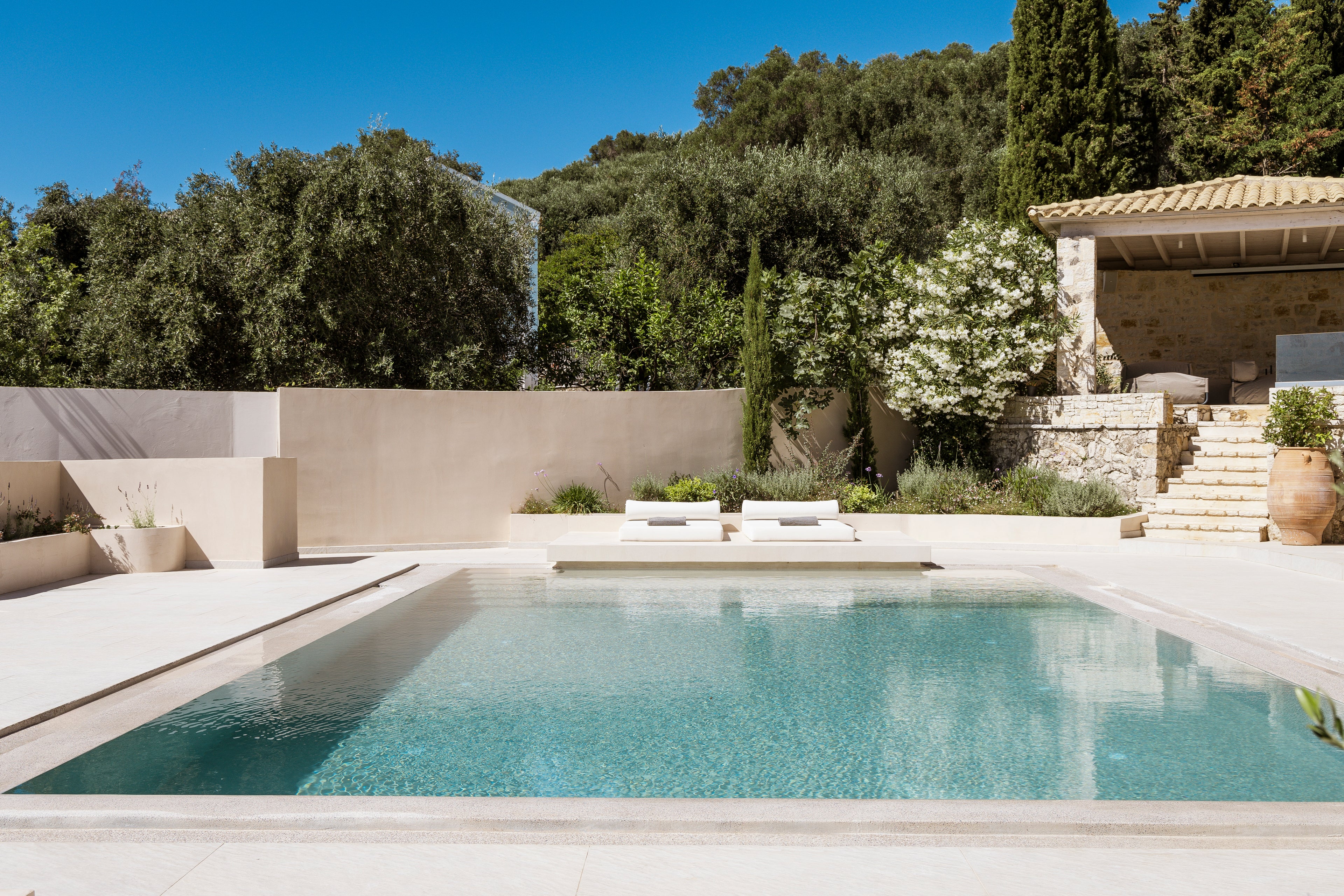 Pool area with lounge chairs, trees, and a clear blue sky